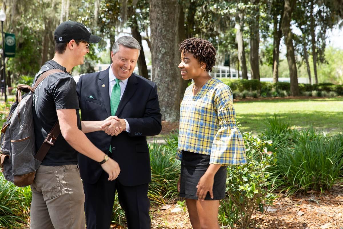 Two students talking with JU President Tim Cost in courtyard on campus