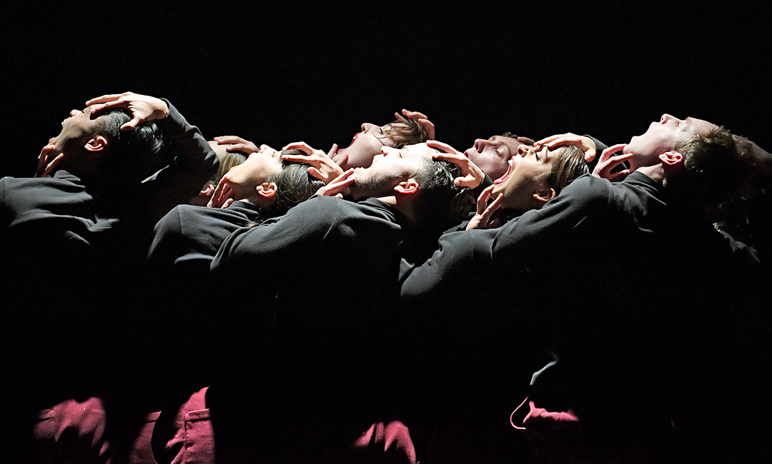 一群身着黑色服装的舞者站在舞台上，舞台上有戏剧性的灯光